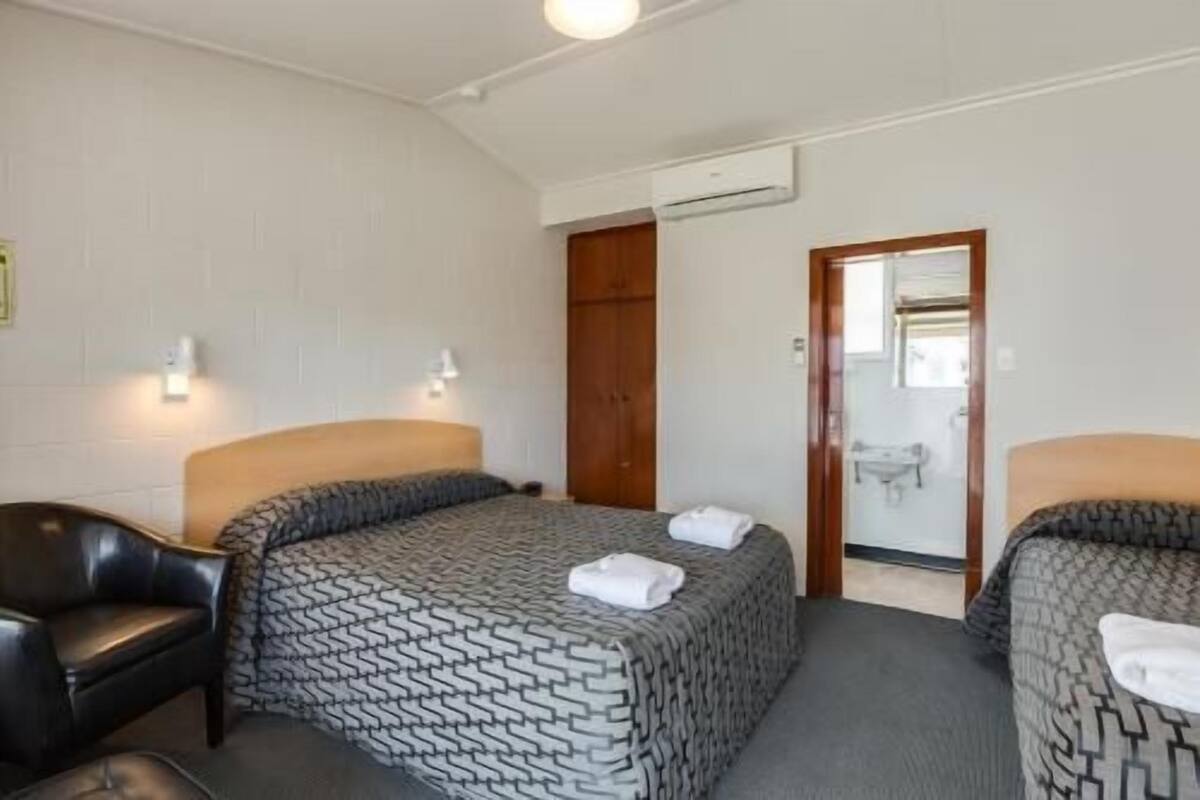 A hotel room with two beds, a wooden wardrobe, a mirror, and a white air conditioning unit.