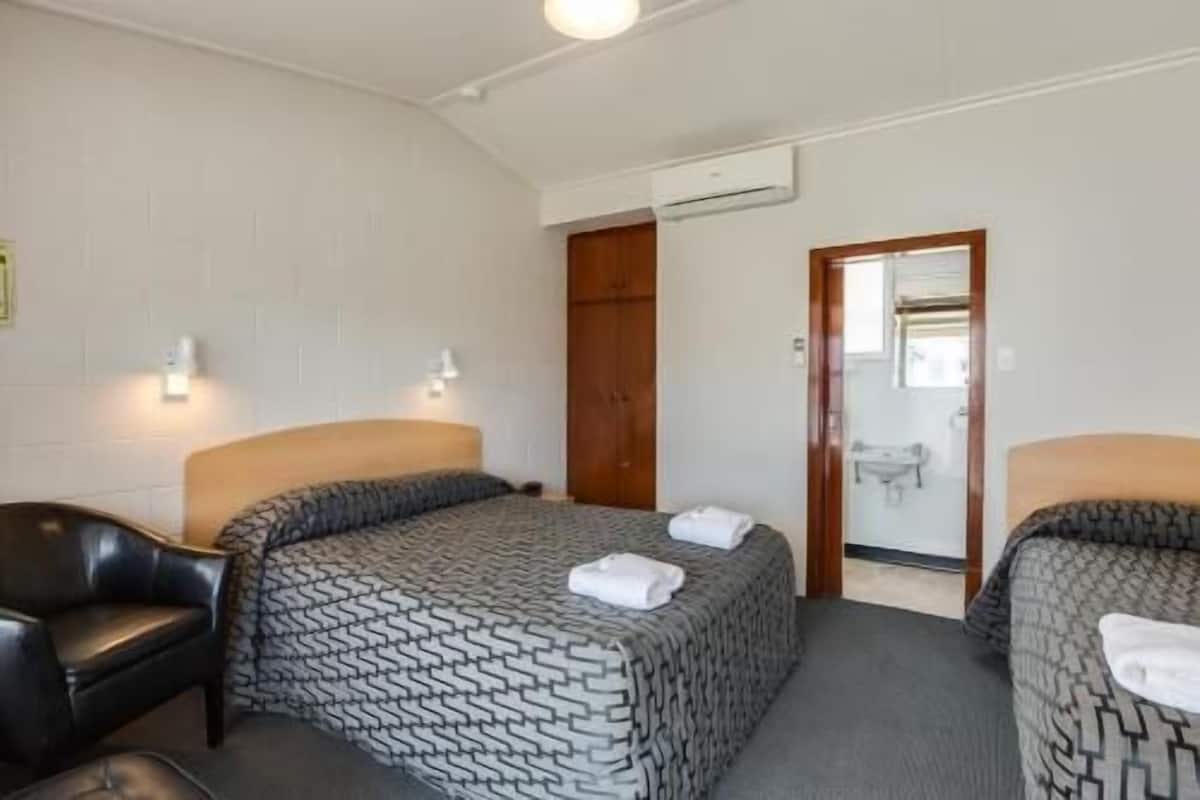 Une chambre d’hôtel avec deux lits, une armoire en bois, un miroir et un appareil de climatisation blanc.