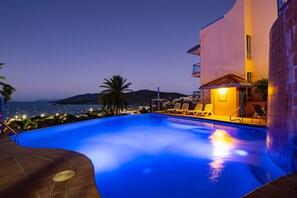 Une piscine à bord incurvé, des chaises longues et une vue sur la mer au crépuscule.