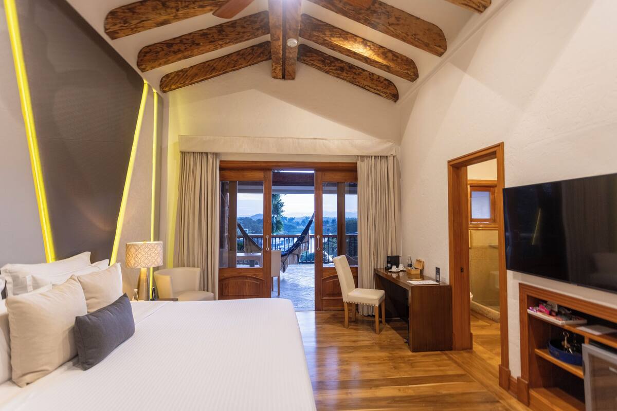 Un dormitorio amplio con una cama grande, un escritorio y un televisor. Cuenta con un balcón con vistas al exterior.