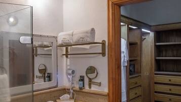 A bathroom with a glass-enclosed shower, wooden vanity, and a walk-in closet with shelves.