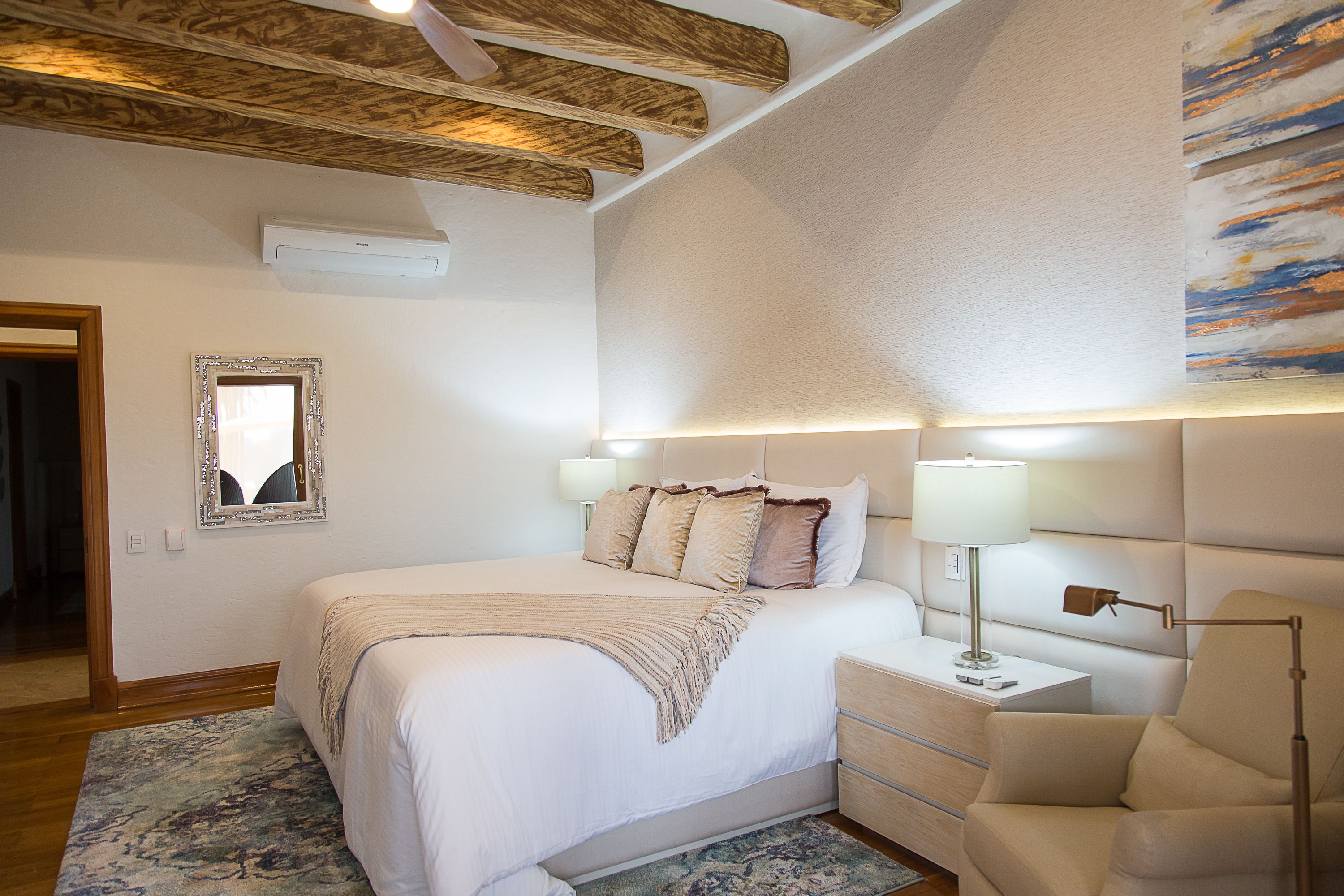 A bedroom with a large bed, bedside lamps, a nightstand, a chair, and a painting on the wall.