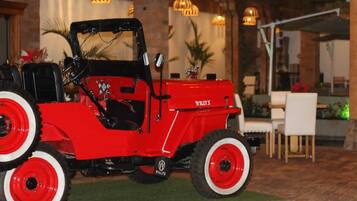A red Willys off-road vehicle parked in an outdoor area with a brick wall and indoor seating in the background.