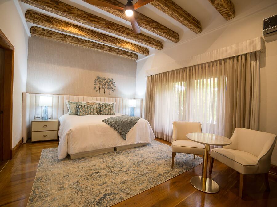 A bedroom with a large bed, bedside tables, a chair, a round table, and a ceiling fan.