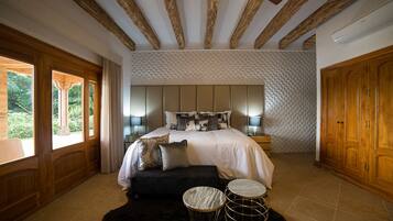 Quarto com cama grande, abajures, teto de madeira e vista para o verde lá fora.