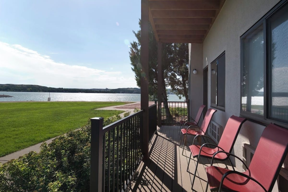 A balcony with red chairs overlooking a lake.