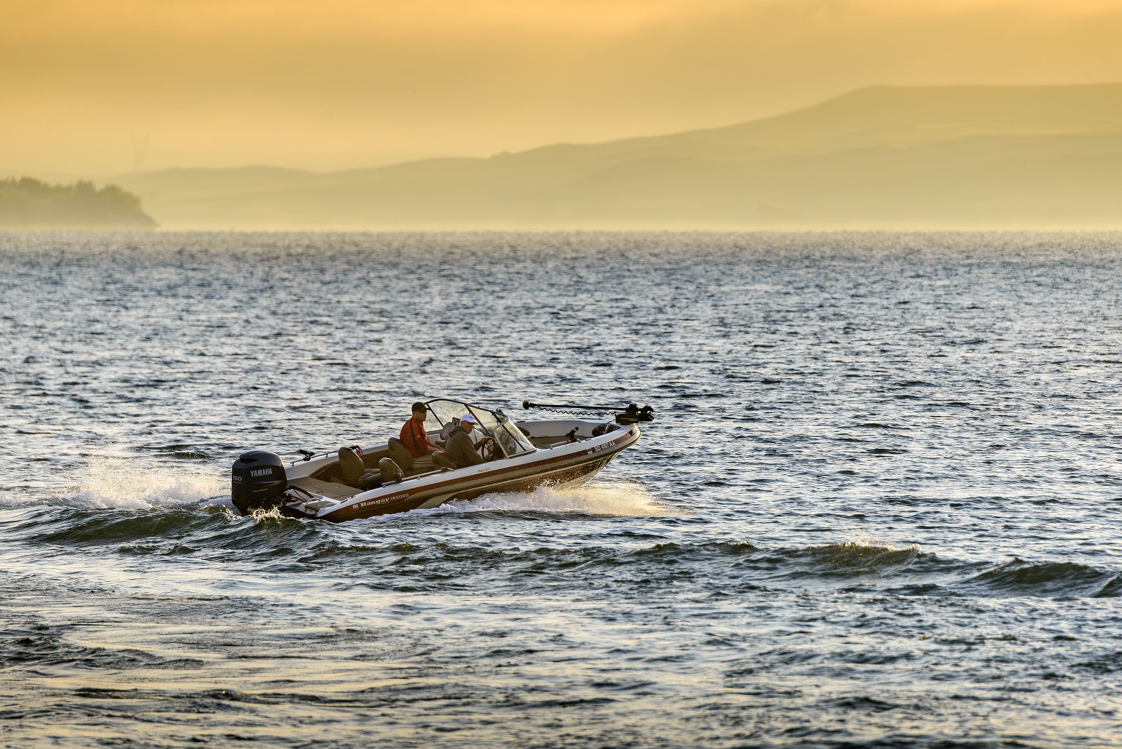 Un petit bateau à moteur sur une étendue d’eau, avec un paysage montagneux en arrière-plan.