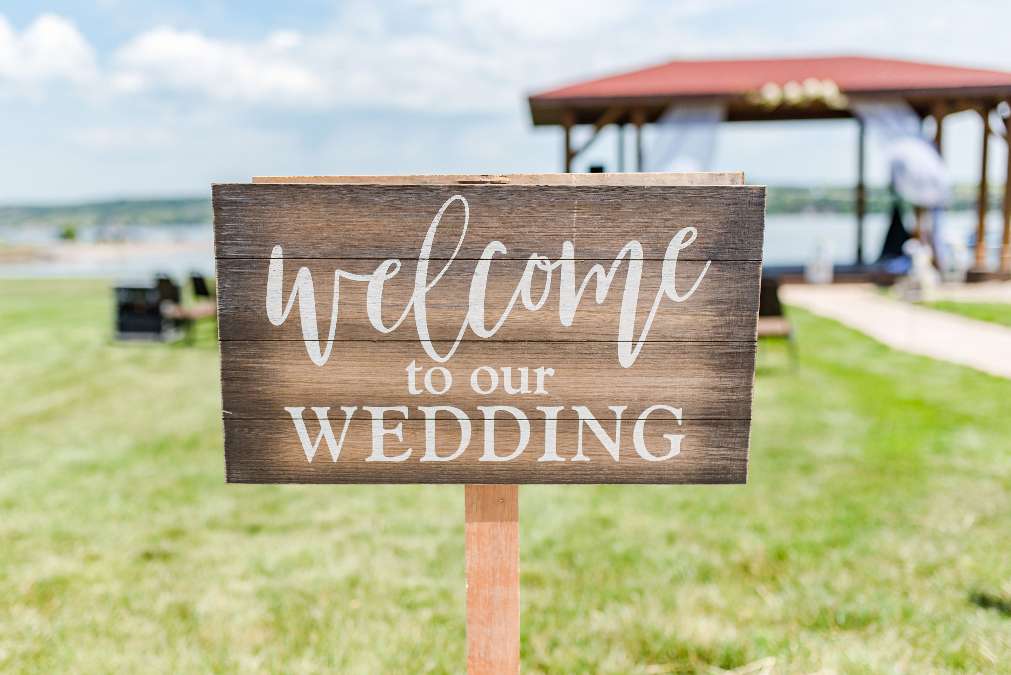 Un letrero de madera con el texto 'welcome to our WEDDING' en letras blancas cursivas.
