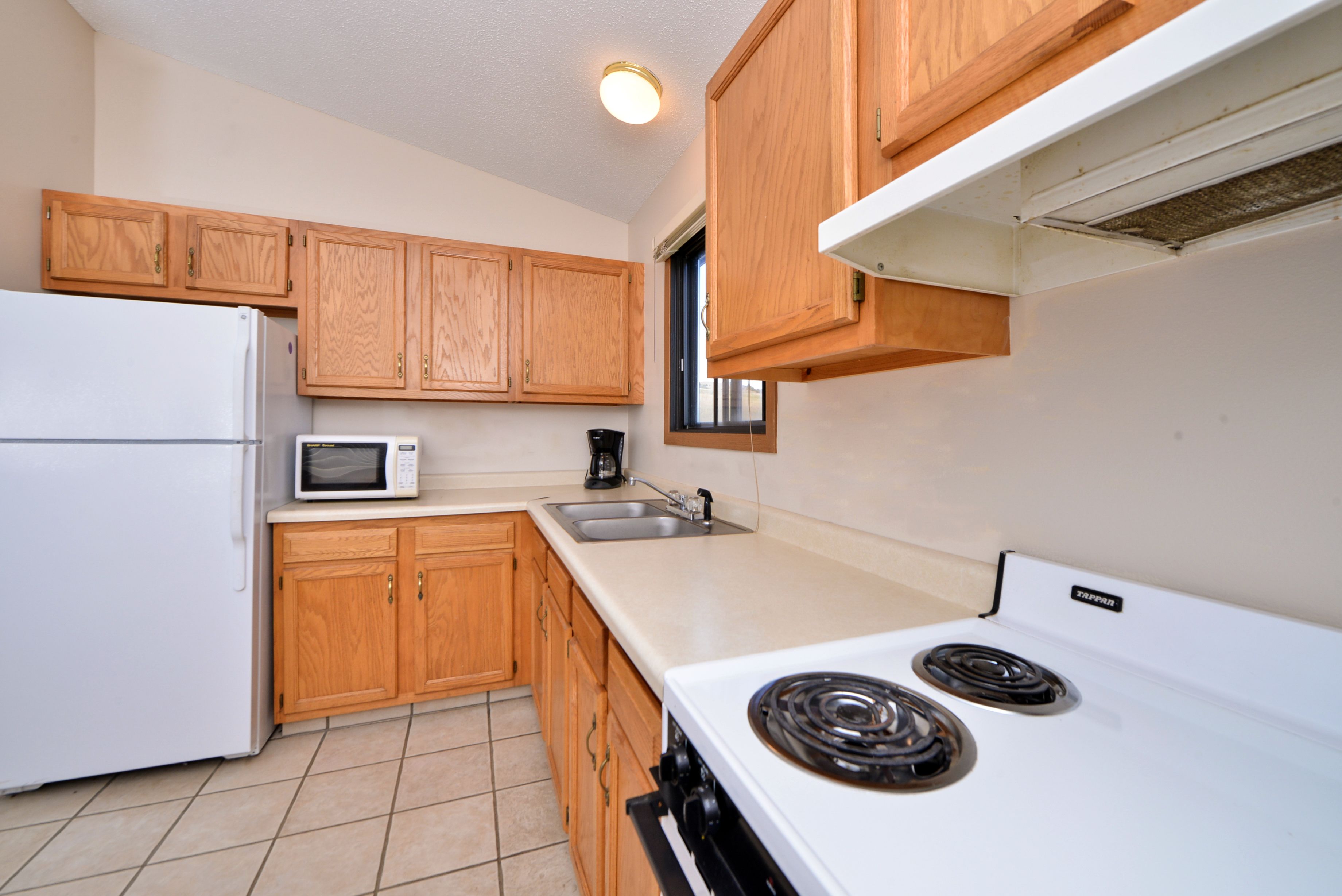 A kitchen with wooden cabinets, a white refrigerator, a microwave, a stove, and a sink.