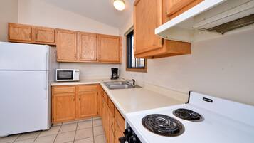 A kitchen with wooden cabinets, a white refrigerator, a microwave, a stove, and a sink.