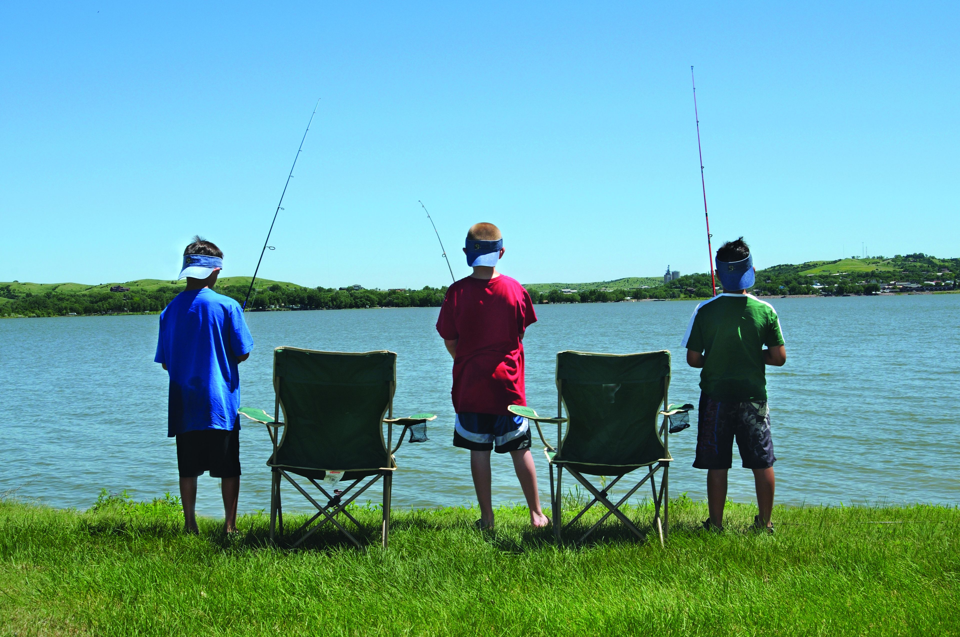 Tres personas pescando en un lago, con sillas y cañas de pescar.