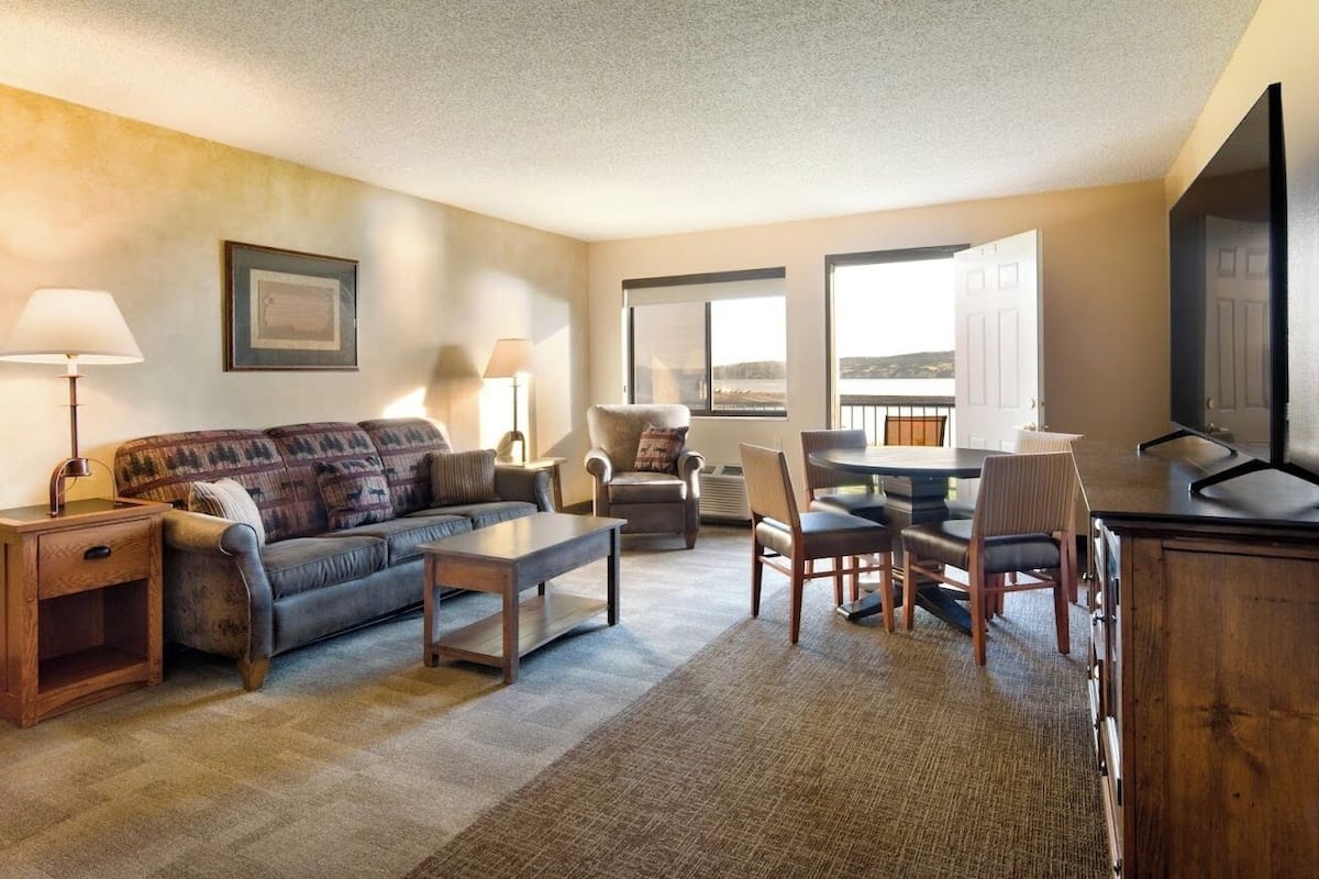 A living room with a sofa, armchairs, a coffee table, a TV, and a dining area with chairs and a table.