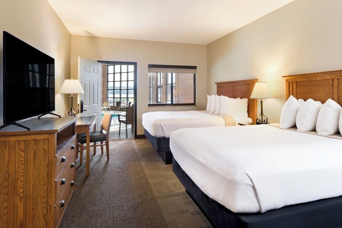 A hotel room with two beds, a desk with a TV, and a view of the outside.