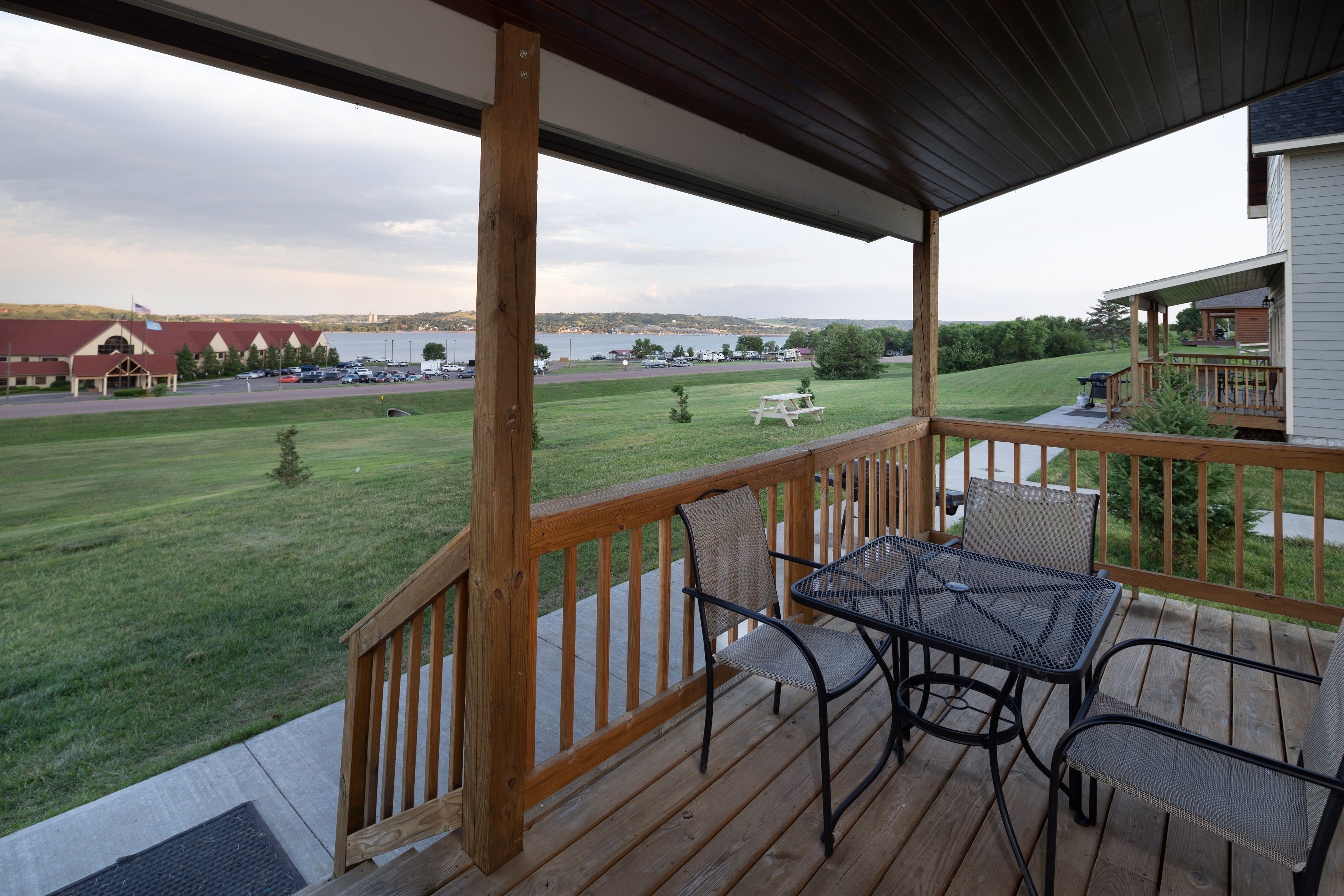 A covered outdoor area with a wooden deck, a table with chairs, and a view of a parking lot and a building across the street.