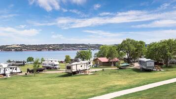 A campground with RVs parked on a grassy field, a small building, and a lake in the background.
