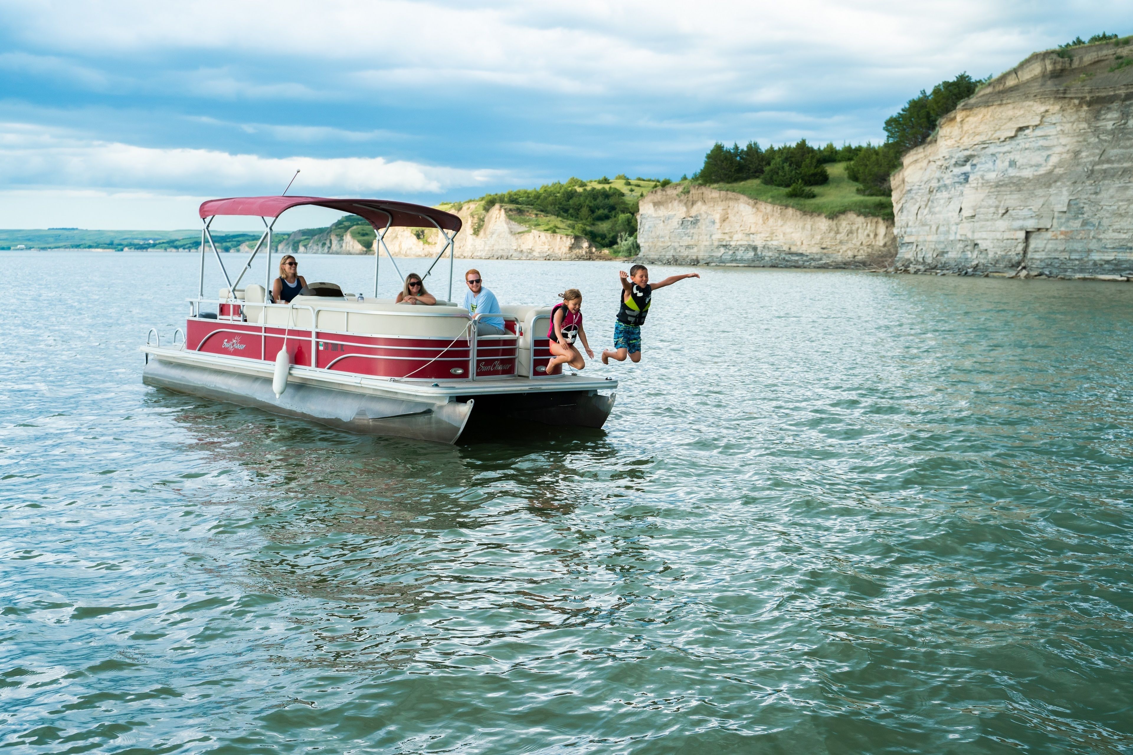 A boat with people on it, a calm body of water, and a cliff in the background.