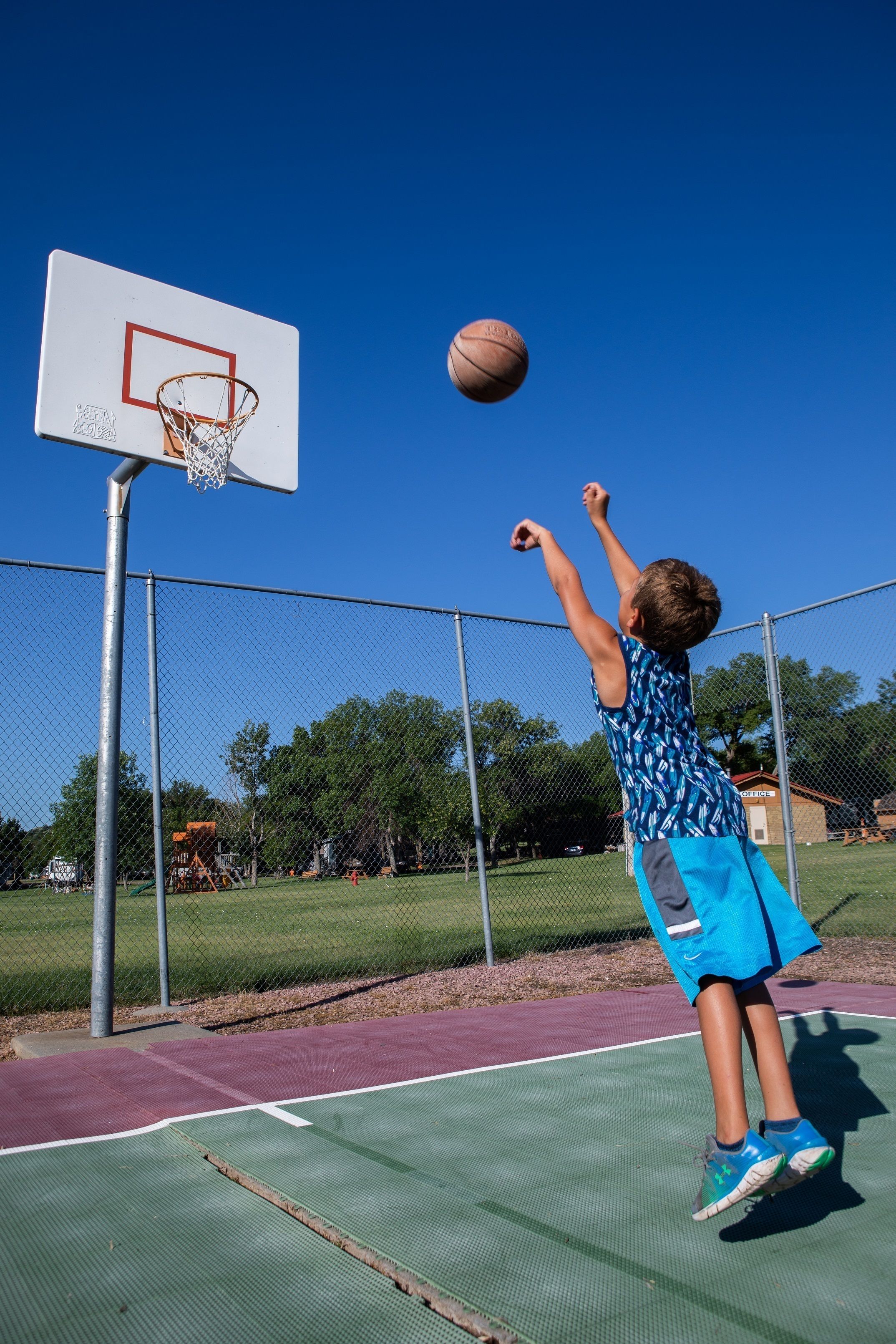 A basketball court with a hoop, a chain-link fence, and a clear blue sky.