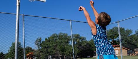 A basketball court with a hoop, a chain-link fence, and a clear blue sky.