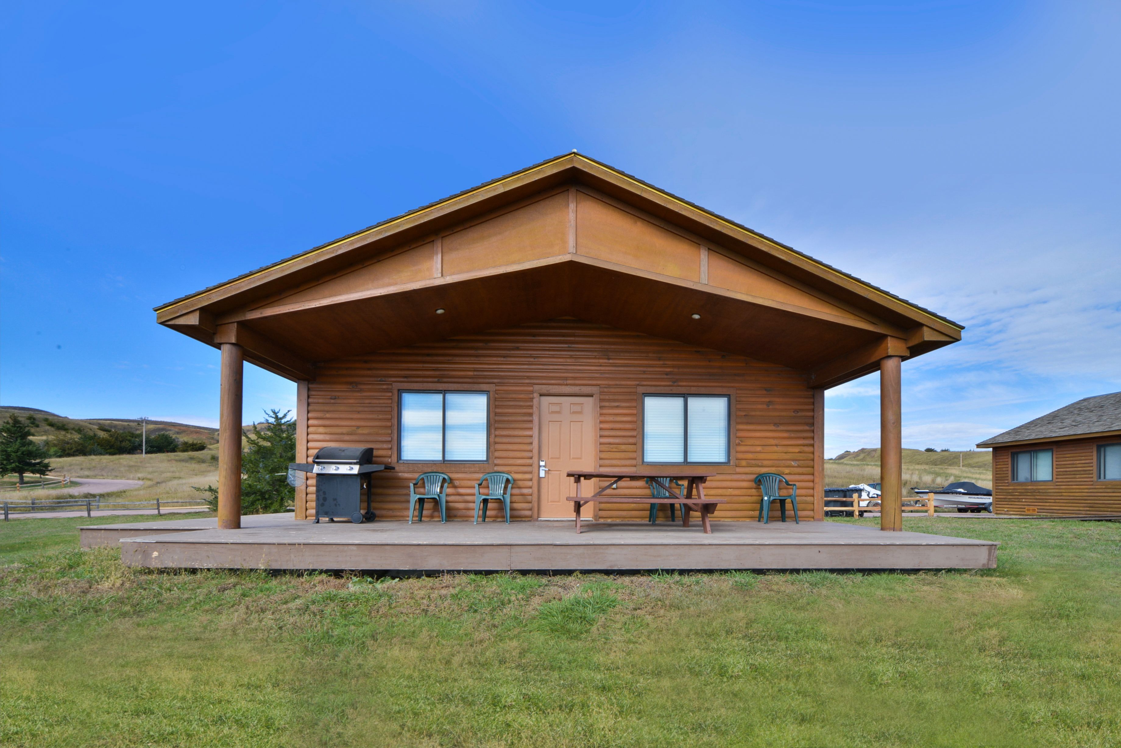 A wooden cabin with a porch, picnic table, and chairs.