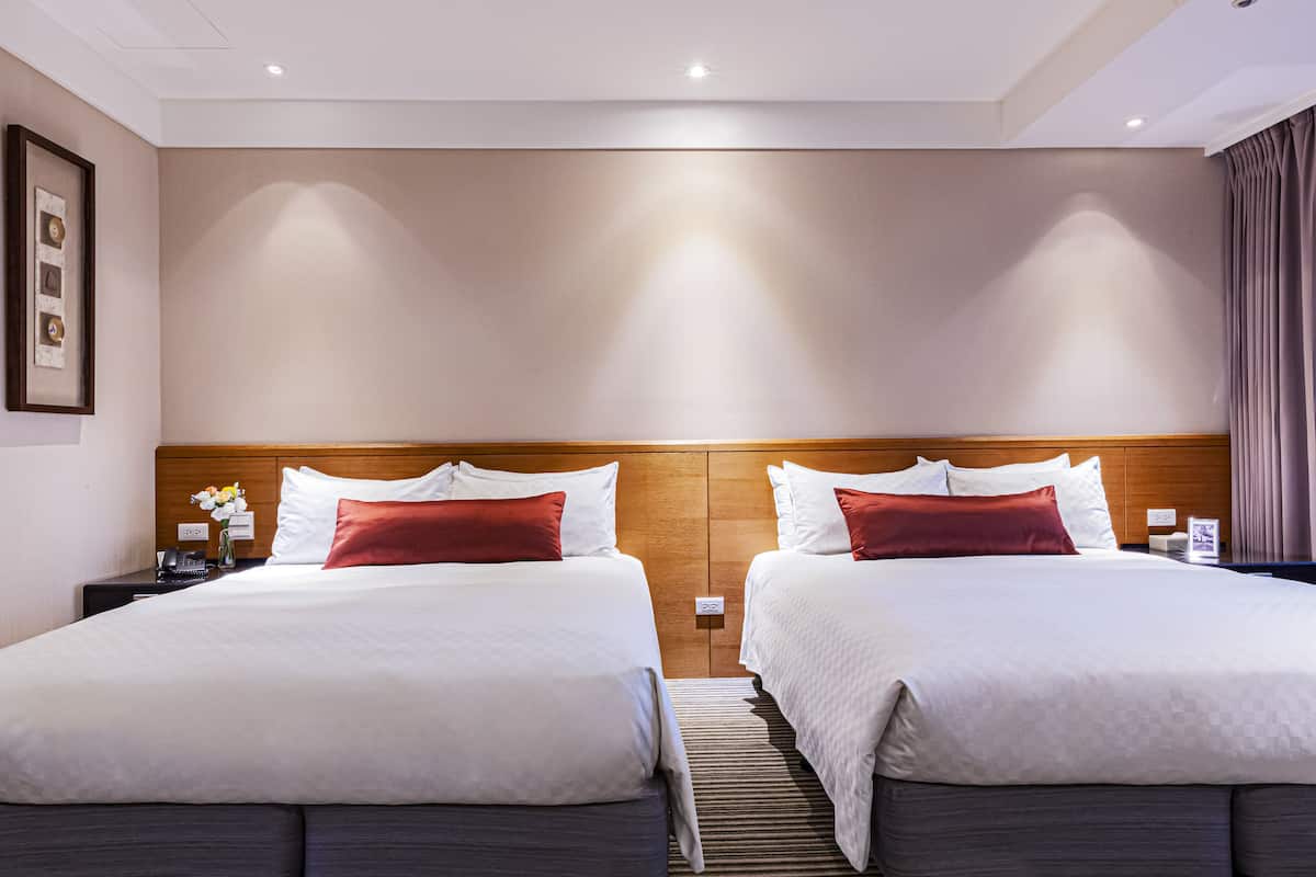 A hotel room with two beds, a wooden headboard, a nightstand with a phone, and a framed picture on the wall.