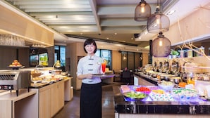 A buffet setup with various food items and a server holding a tray.