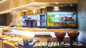 Uma área de buffet com diversos alimentos e uma geladeira repleta de frutas e legumes.