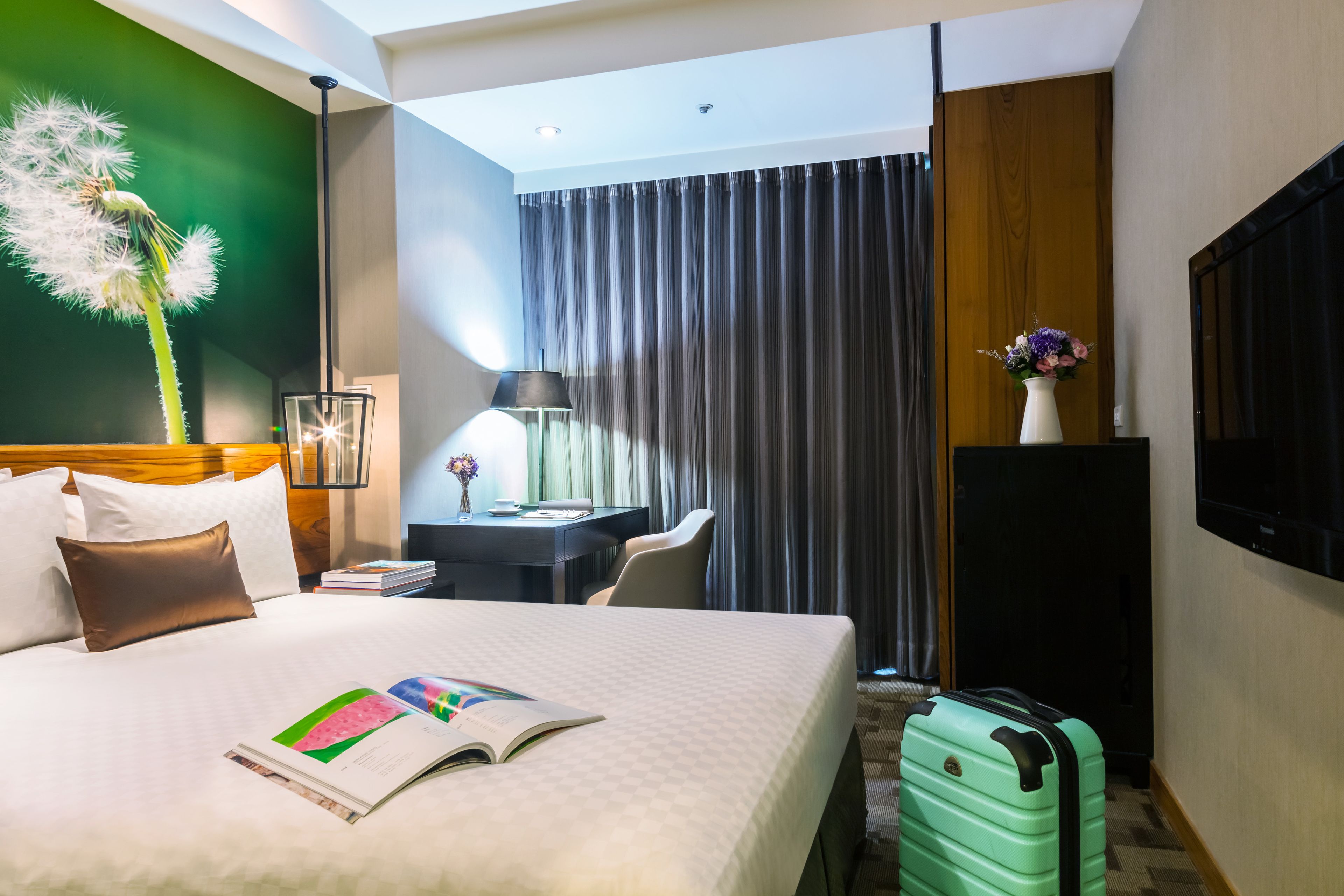 A hotel room with a bed, a desk, a chair, a lamp, a TV, and a suitcase.