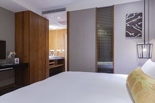 Habitación de hotel con una cama grande, un armario de madera, un baño con lavamanos y espejo, y un cuadro en la pared.