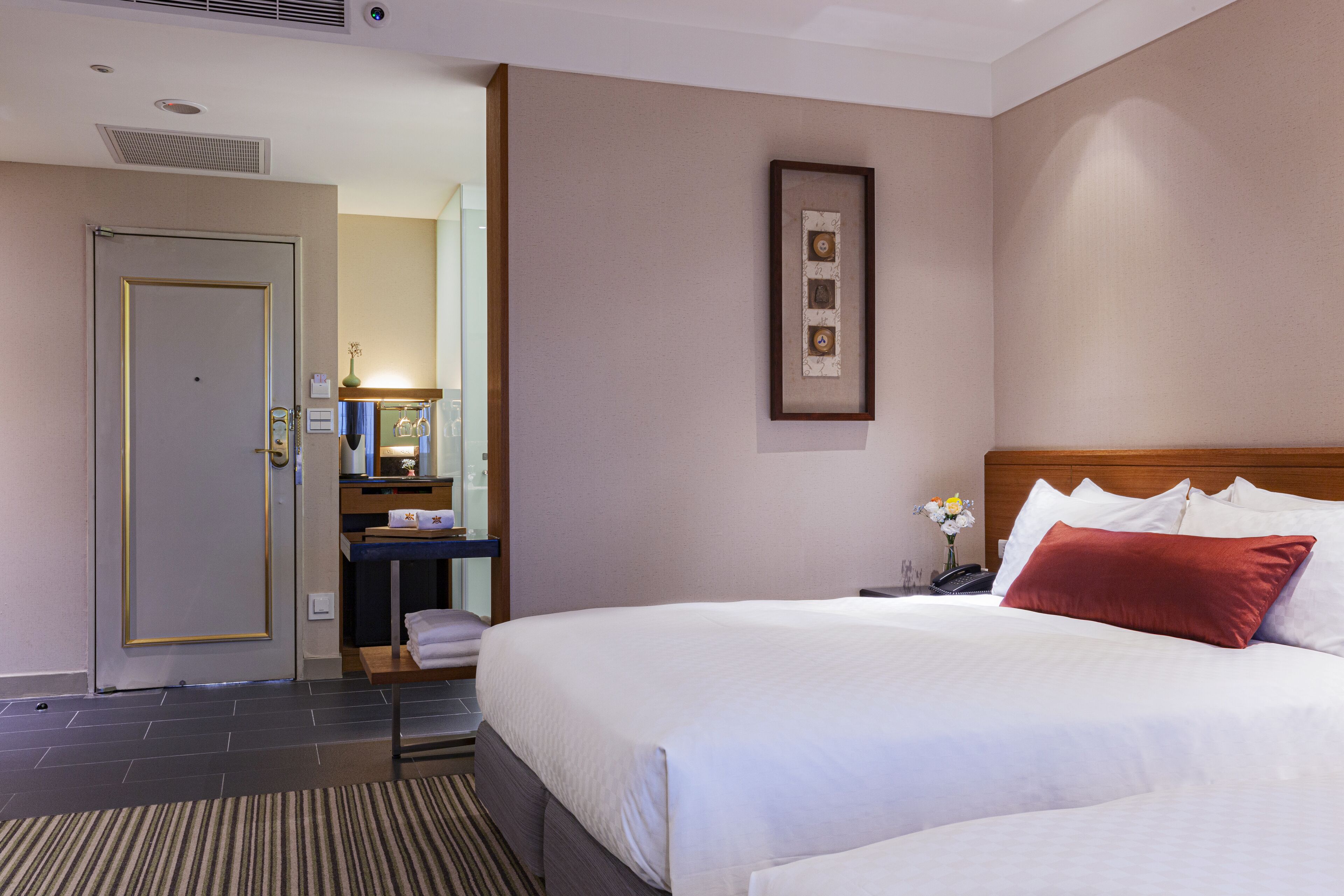 A hotel room with a large bed, a wooden headboard, a bedside table with a lamp, a framed picture on the wall, and a door leading to a bathroom.