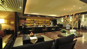 A modern hotel lobby with a reception desk, seating area, and decorative plants.