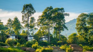 A riverside property with multiple houses surrounded by dense greenery and mountains in the background. - The River Resort (Champasak)