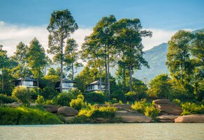Una propiedad a orillas del río con varias casas rodeadas de abundante vegetación y montañas al fondo.