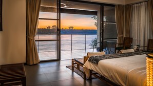A bedroom with a large sliding glass door leading to a balcony, a bed, a desk, and a chair. - The River Resort (Champasak)