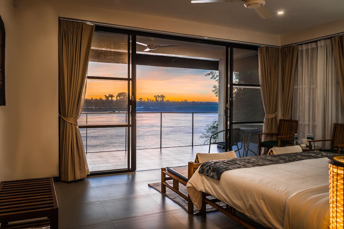 A bedroom with a large sliding glass door leading to a balcony, a bed, a desk, and a chair.