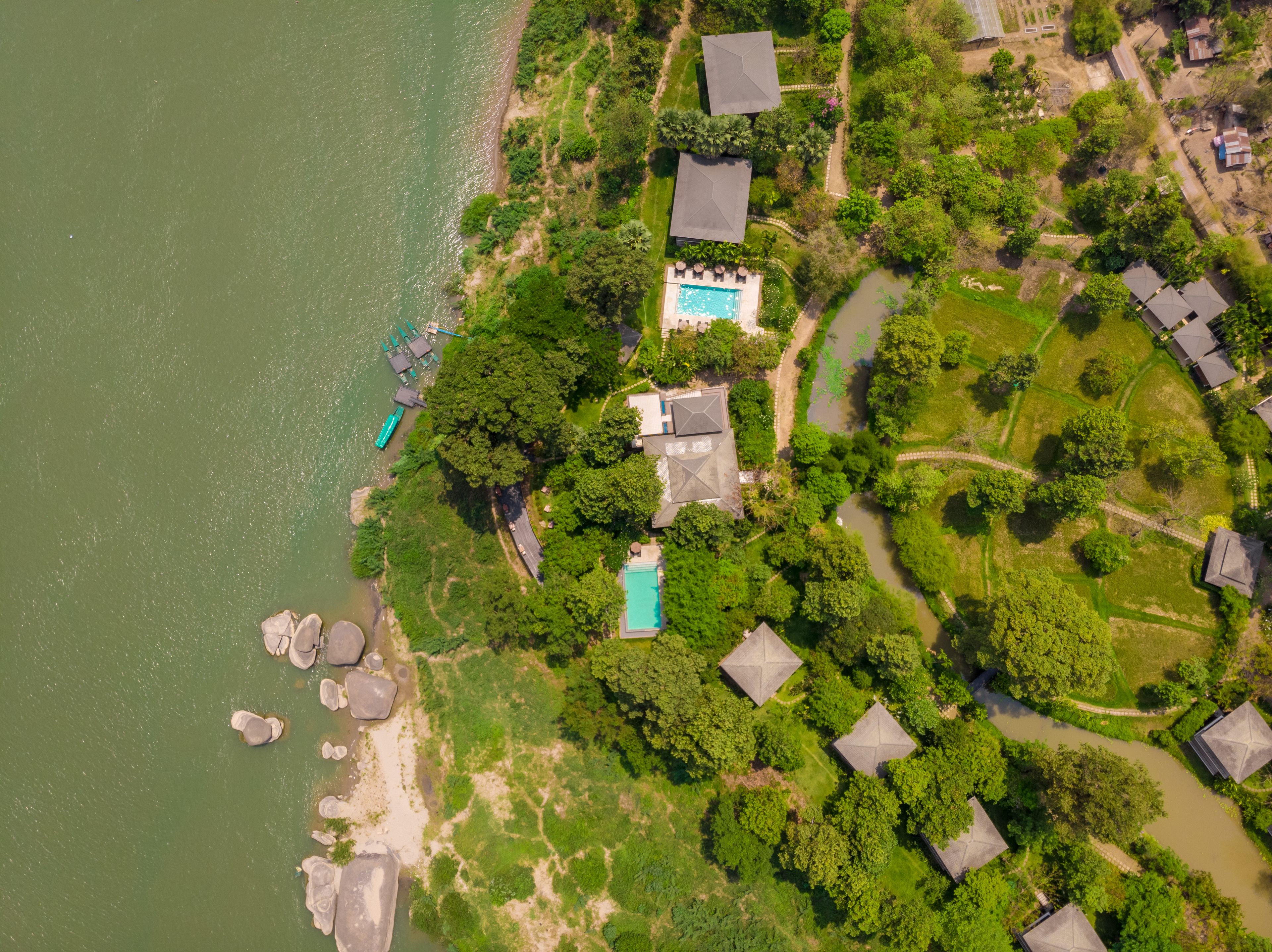 An aerial view of a residential area with houses, a swimming pool, and a river.