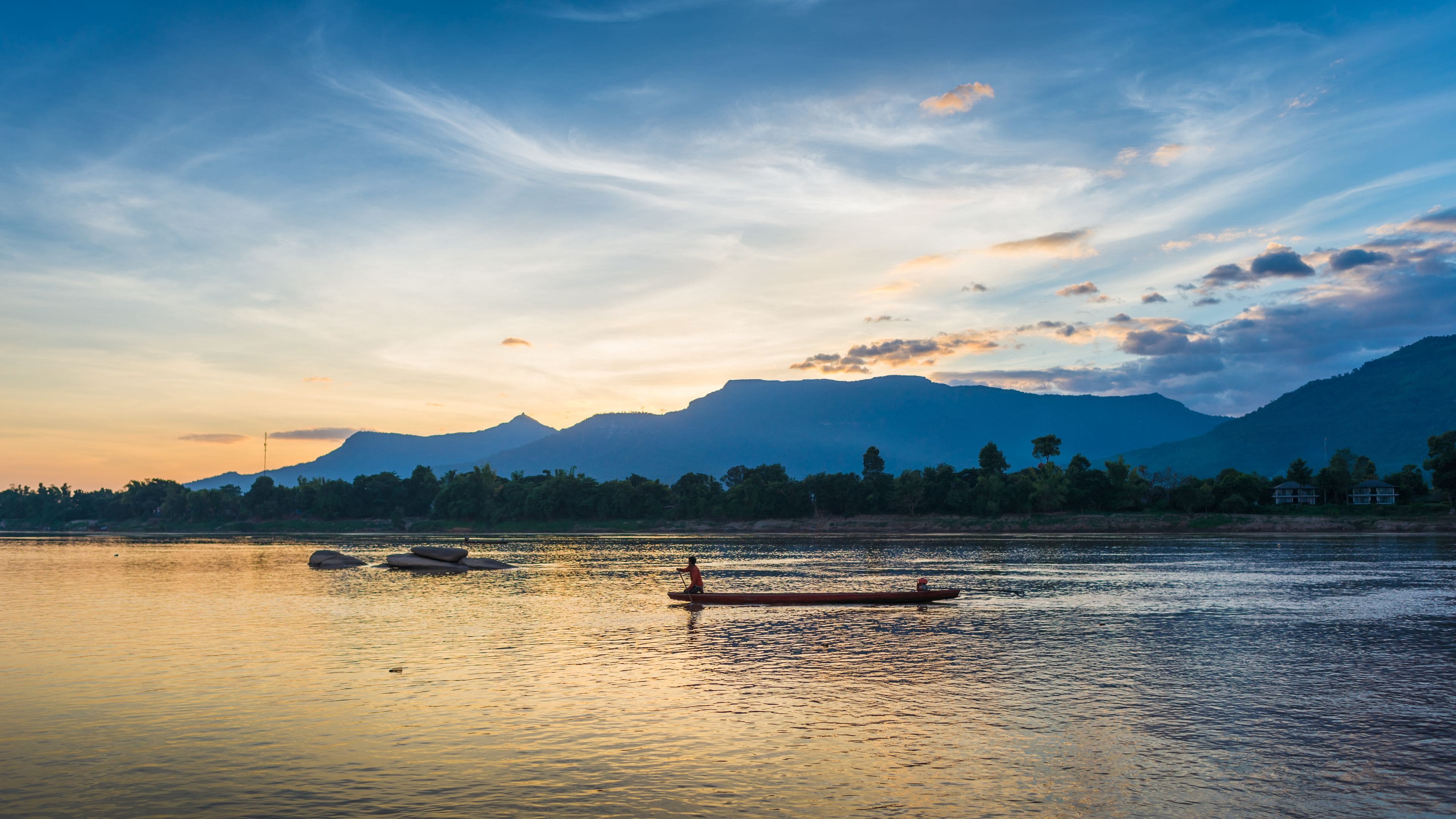 A calm lake with a mountain range in the background and a person fishing in the foreground.