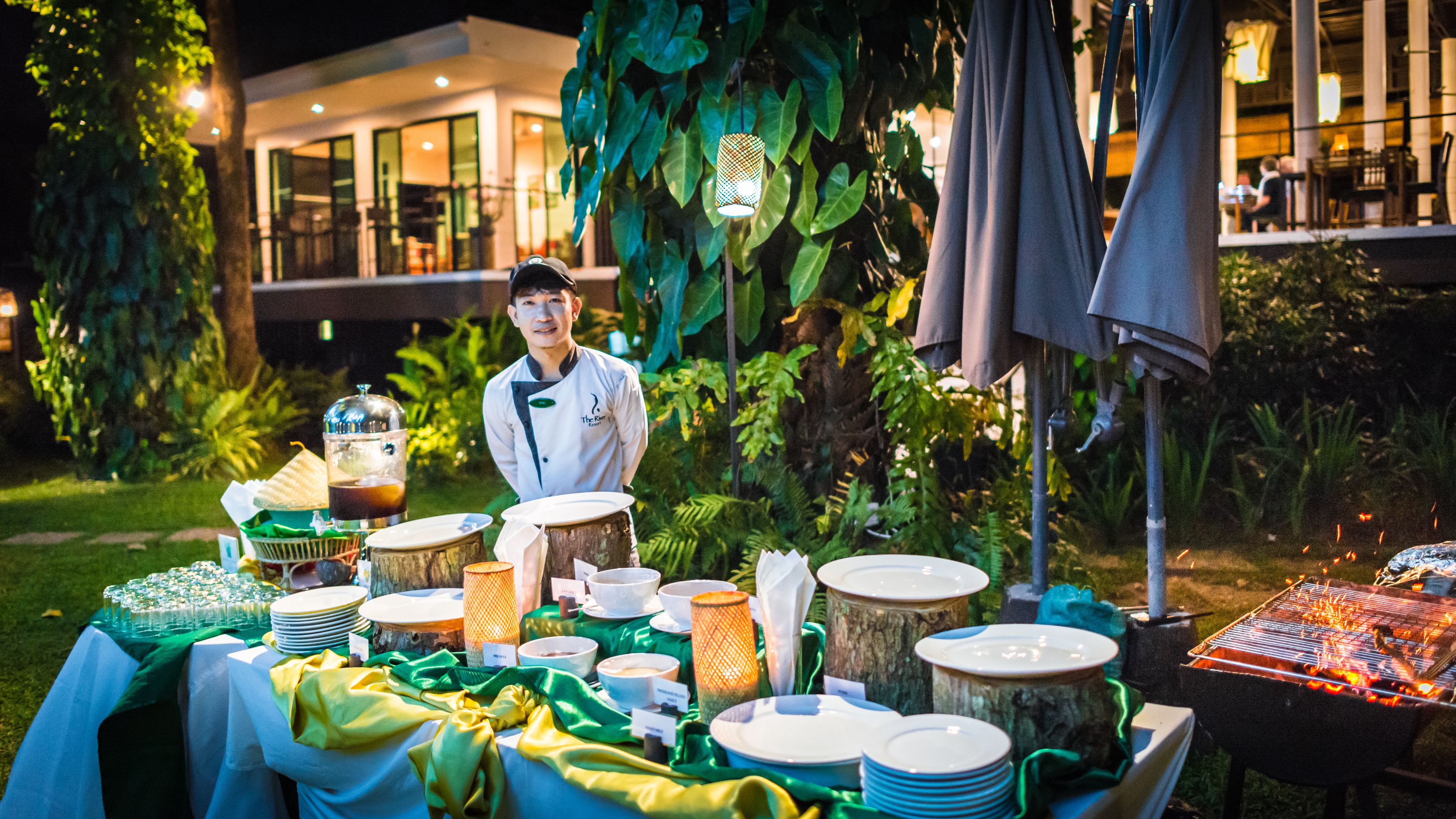 A buffet setup with a variety of dishes and drinks, a grill, and a waiter.