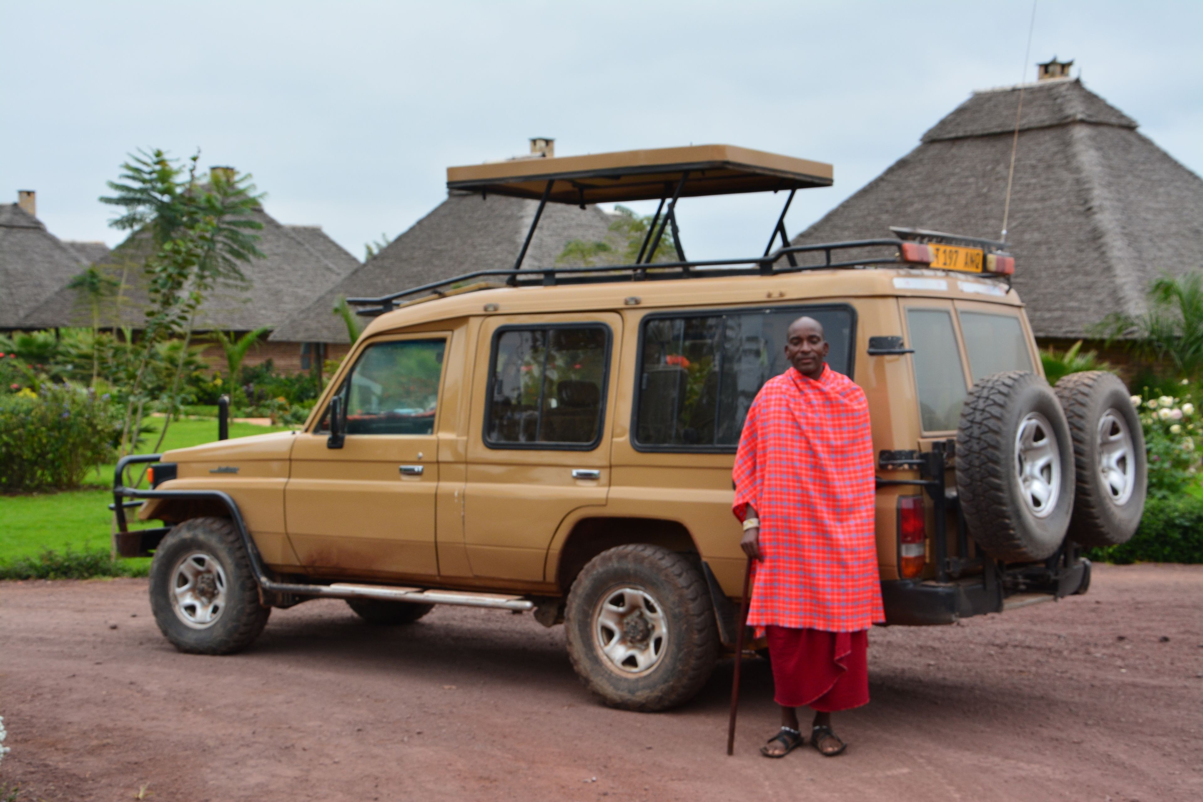 A safari vehicle parked in a rural setting with thatched-roof huts in the background.
