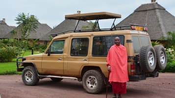 A safari vehicle parked in a rural setting with thatched-roof huts in the background.