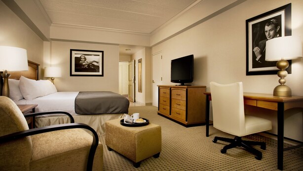Habitación de hotel con cama, escritorio, silla, televisor, cómoda y una pequeña mesa con bandeja.