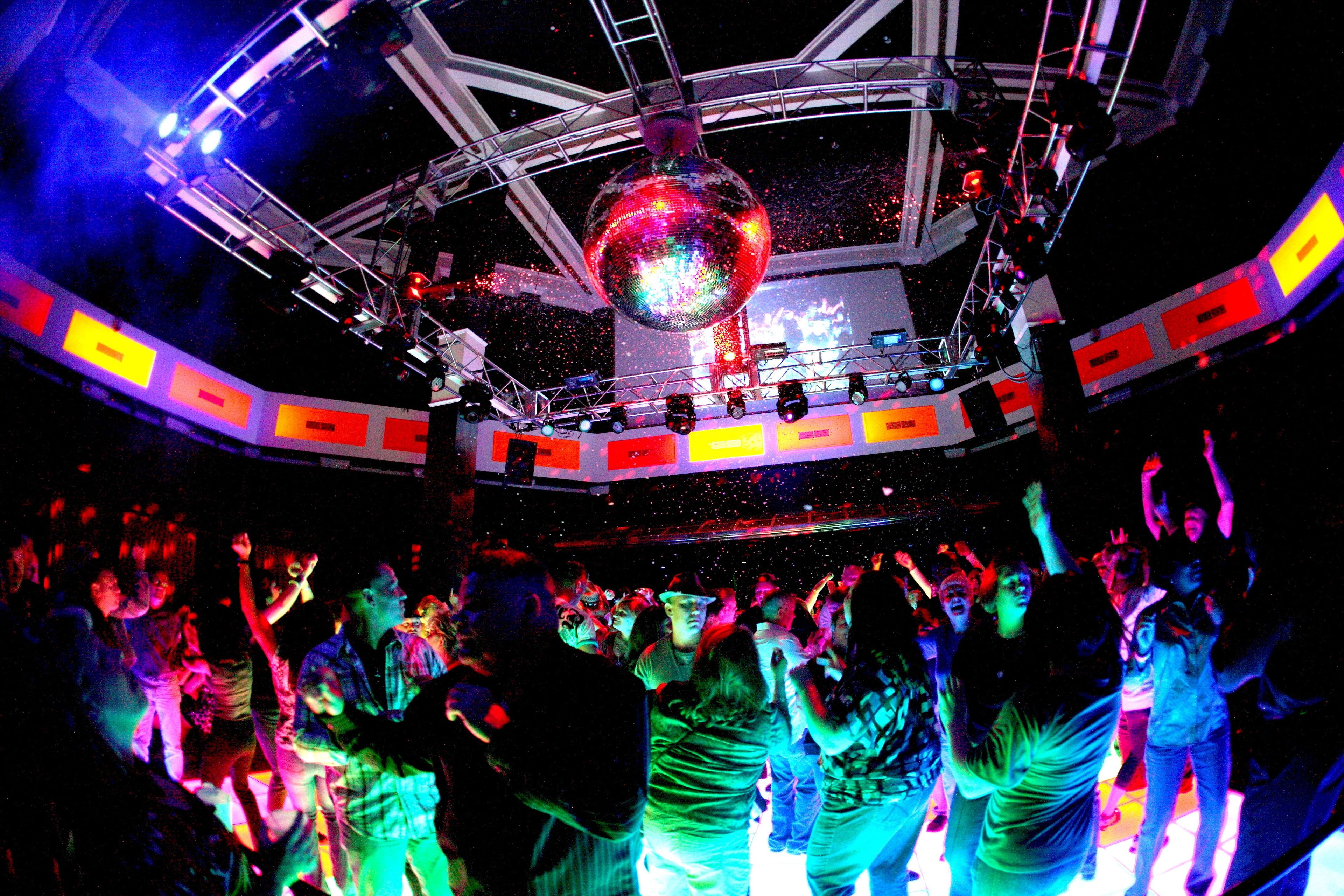 A crowded dance floor with a disco ball overhead.