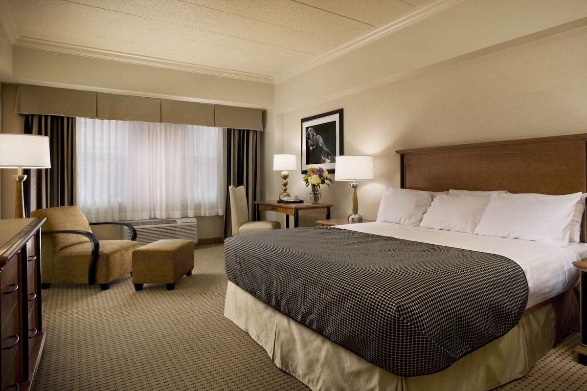 A hotel room with a large bed, two bedside tables, a desk, a chair, and a window with curtains.