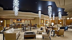 Un vestíbulo amplio con una zona de bar, diferentes disposiciones de asientos y modernos candelabros.