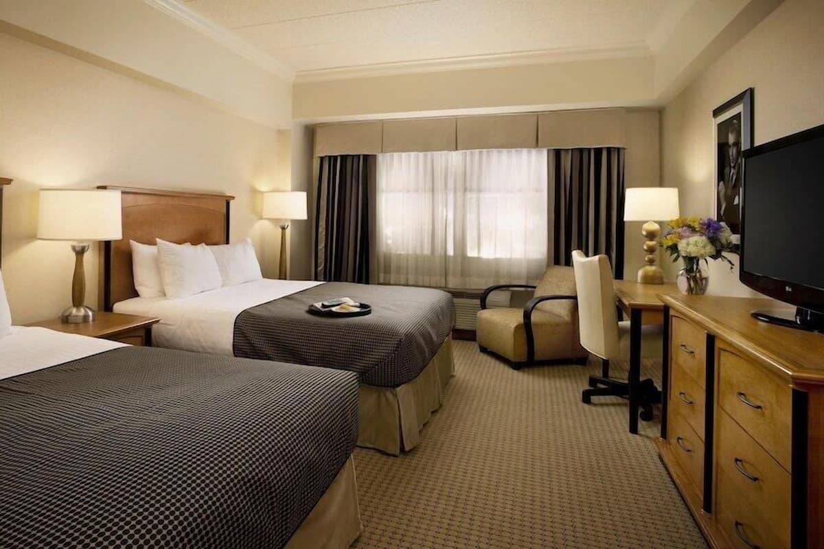 A hotel room with two beds, a desk with a television, and a chair.