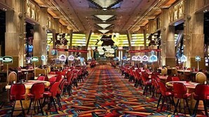 Un salón imponente con filas de sillas y mesas rojas, detalles ornamentales en el techo y una alfombra colorida.