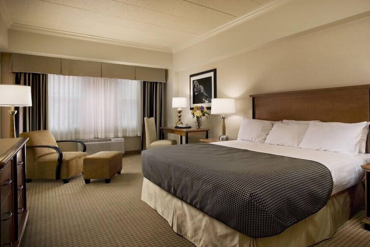 A hotel room with a large bed, a desk, a chair, a nightstand, and a wall-mounted picture.