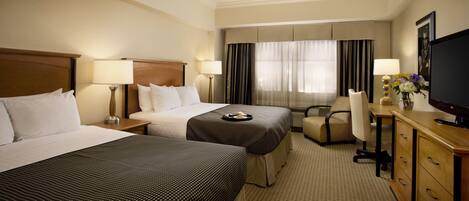 Une chambre d’hôtel avec deux lits, un bureau, une chaise, une télévision et une commode.