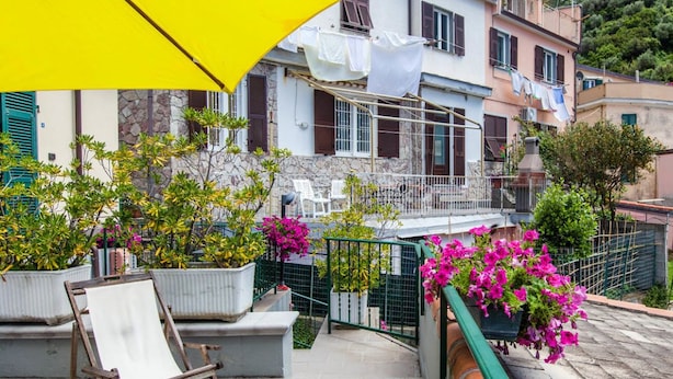 A balcony with a yellow umbrella, potted plants, and a chair. - Hotel del Sole (Riomaggiore)