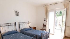 A bedroom with two beds, a small table, a chair, and a view of the outside through a door. - Hotel del Sole (Riomaggiore)
