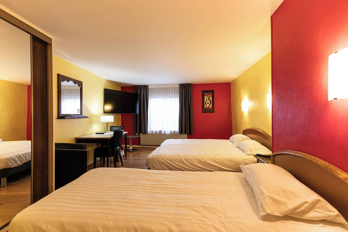 A hotel room with two beds, a desk with a chair, a TV, and a window with curtains.